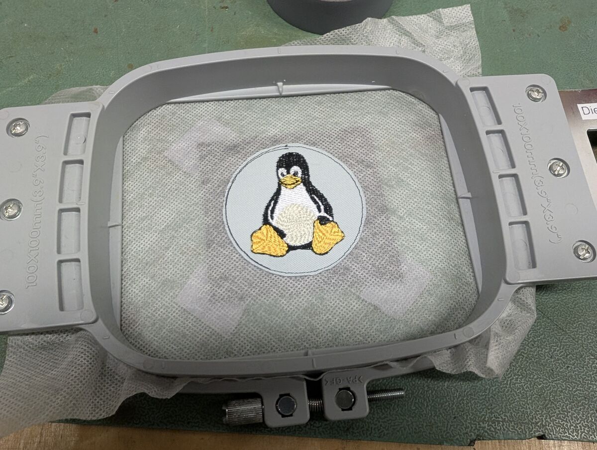 Vorderseite mit fertig gesticktem Tux auf hellblauem Grund, noch ohne umlaufenden Rand