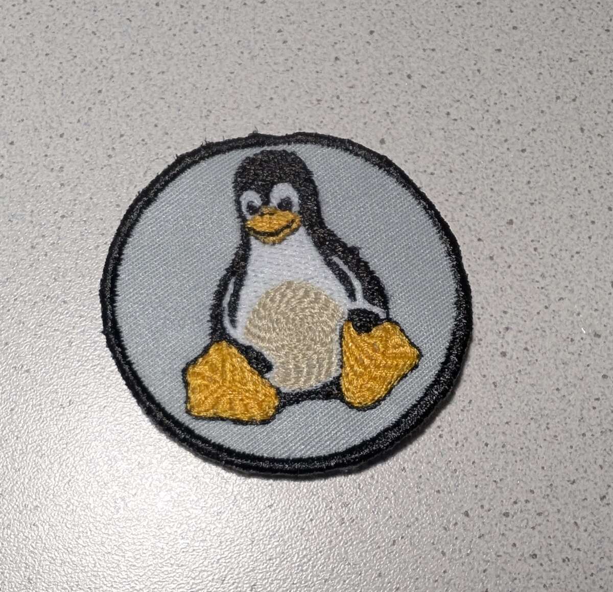 Das fertige, ausgewaschene Patch mit Tux und schwarzem Satinrand liegt auf einer hellen Arbeitsfläche